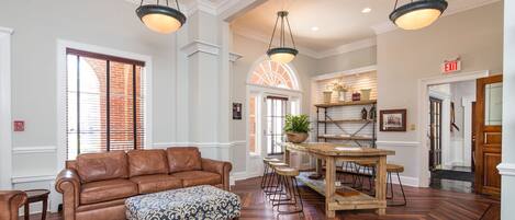 A spacious lobby with a brown leather sofa, patterned ottoman, and a wooden dining table with bar stools.
