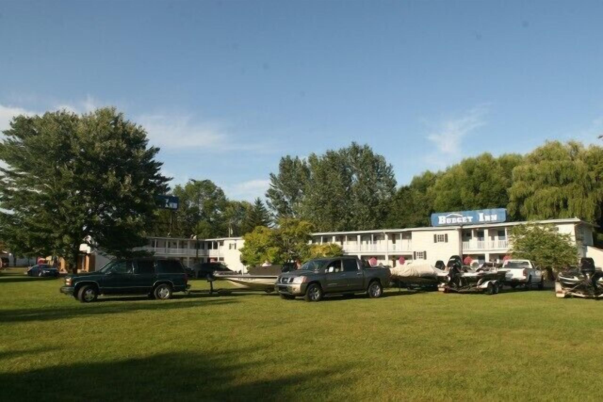 Un motel con un amplio jardín, un letrero que dice 'Budget Inn' y varios vehículos estacionados.