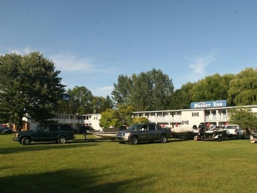 Un motel con un amplio jardín, un letrero que dice 'Budget Inn' y varios vehículos estacionados.