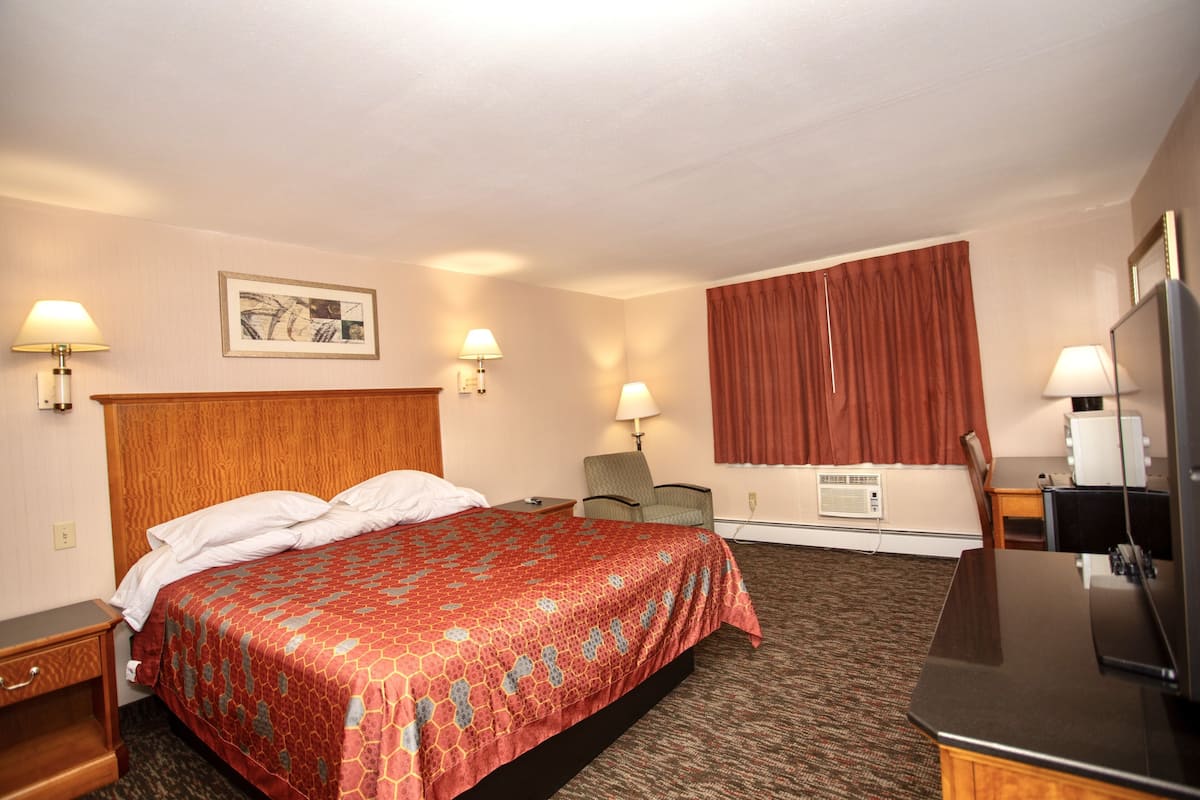 A hotel room with a large bed, two bedside tables, a desk with a chair, a television, and two wall-mounted lamps.