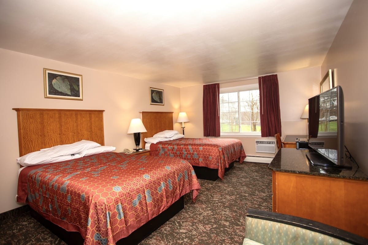 A hotel room with two beds, a TV, a desk, and a window with curtains.