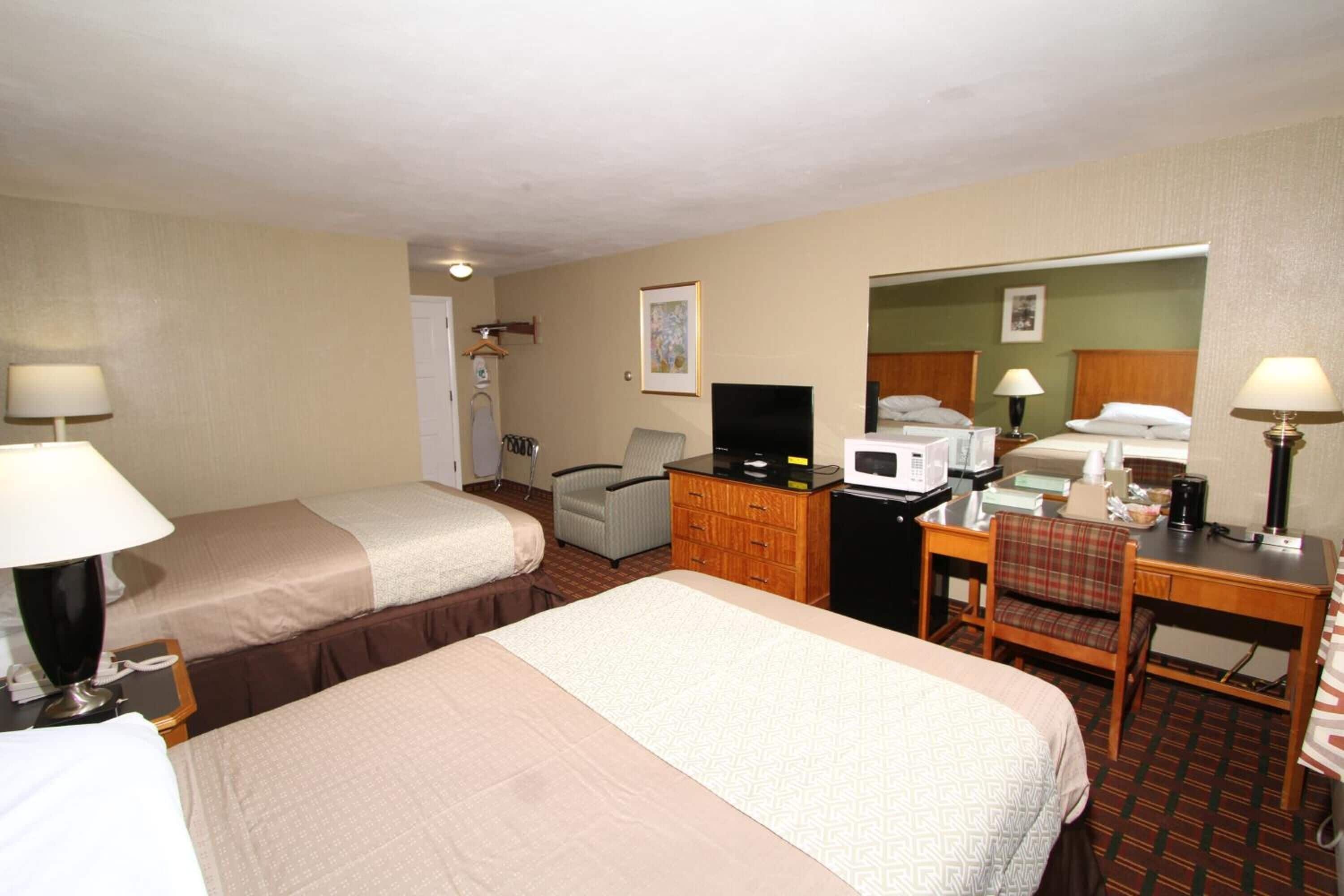 Ein Hotelzimmer mit zwei Betten, einem Schreibtisch, einem Sessel, einem Fernseher, einer Mikrowelle und einem Schminktisch.