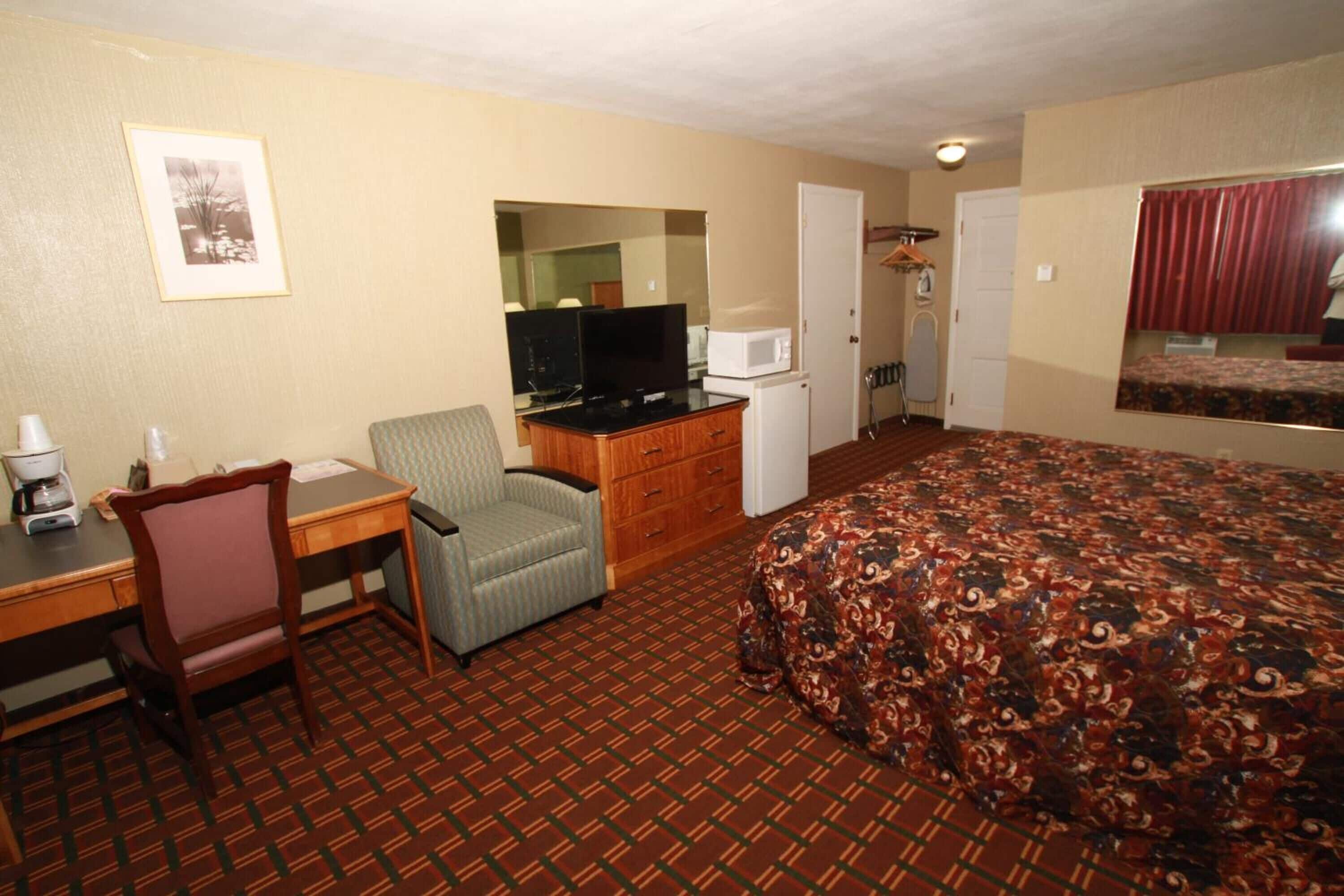 Habitación de hotel con cama, escritorio con silla, televisión, microondas y refrigerador pequeño.