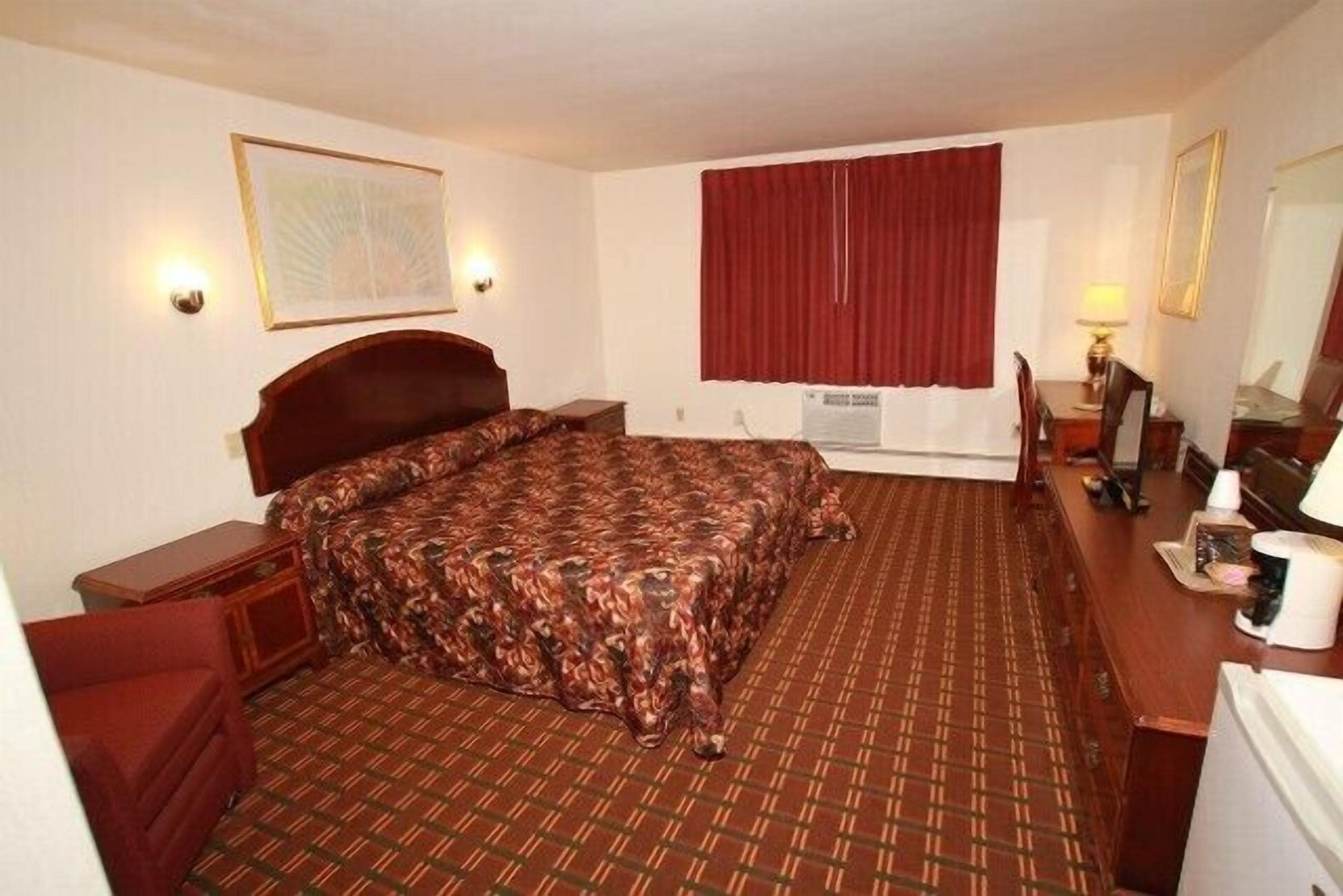 Une chambre d’hôtel avec un grand lit, un bureau avec une chaise, une télévision et une fenêtre avec des rideaux rouges.