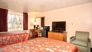 Ein Hotelzimmer mit zwei Betten, einem Schreibtisch mit Computer, einem Fernseher und einem Sessel.