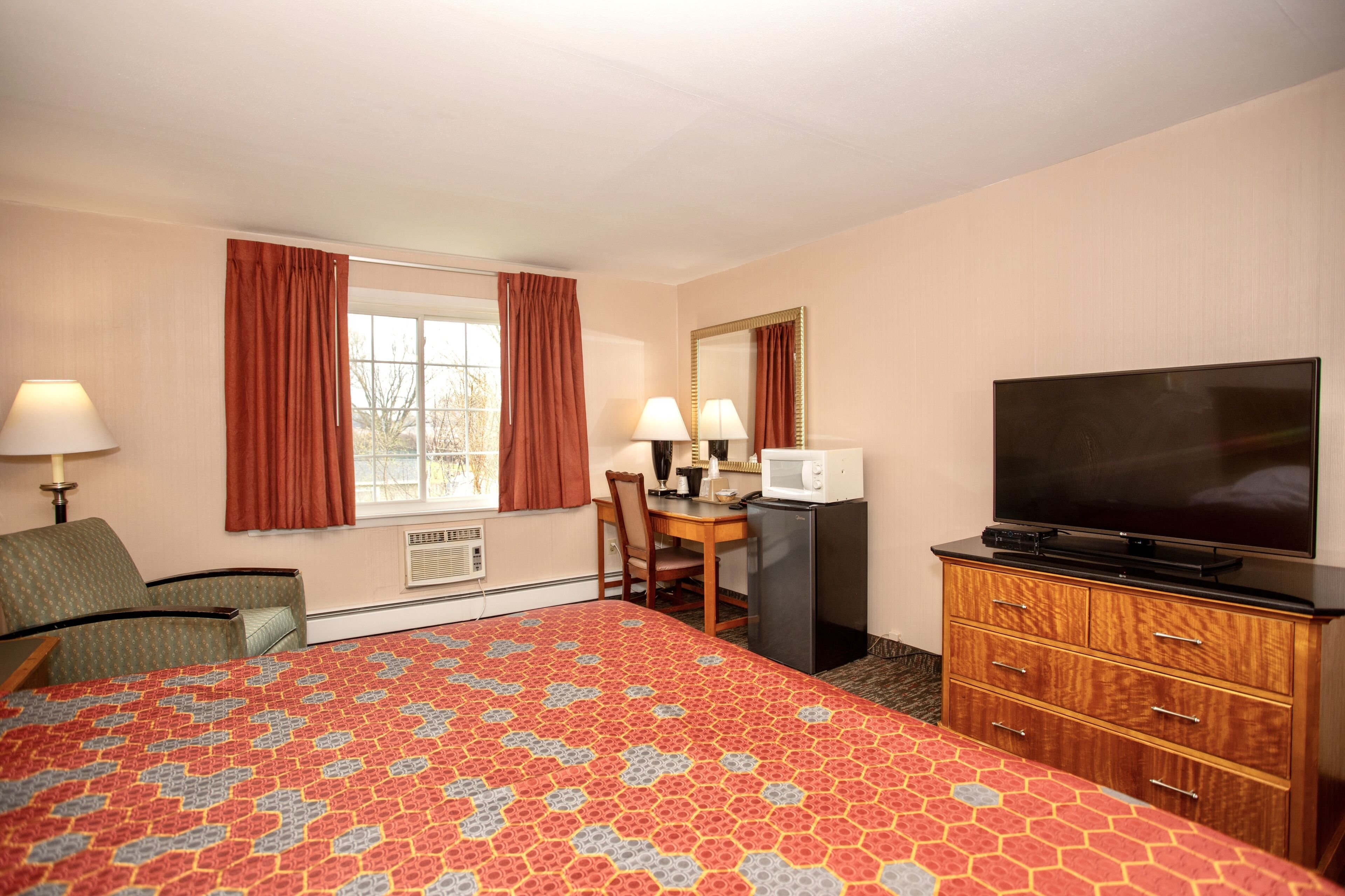 A hotel room with a bed, a desk, a television, and a dresser.