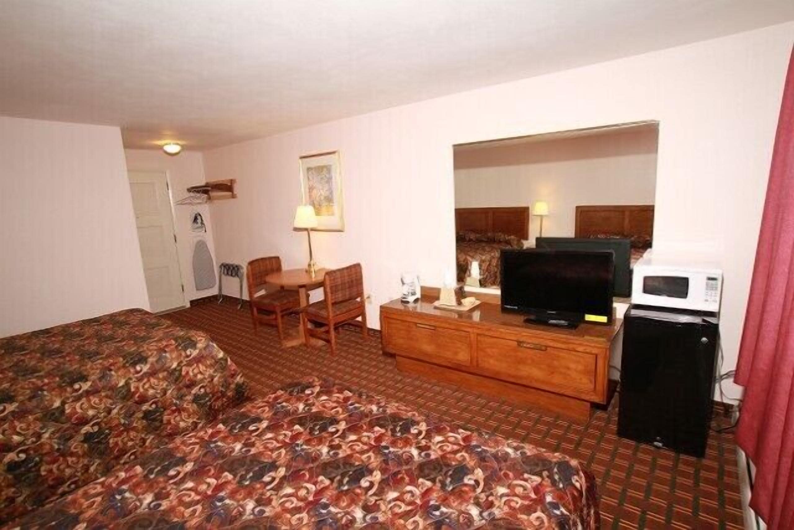 A hotel room with a bed, a TV, a microwave, a desk with a chair, and a small kitchenette.
