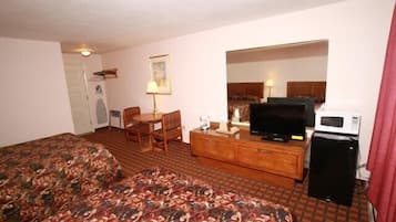 A hotel room with a bed, a TV, a microwave, a desk with a chair, and a small kitchenette.