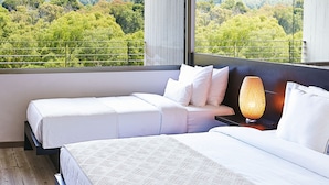 Une chambre d’hôtel avec deux lits, une grande fenêtre donnant sur un paysage boisé et une table de chevet avec une lampe.
