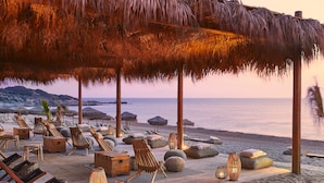 Un salon de plage doté de parasols en chaume, de chaises longues et de tables en bois.