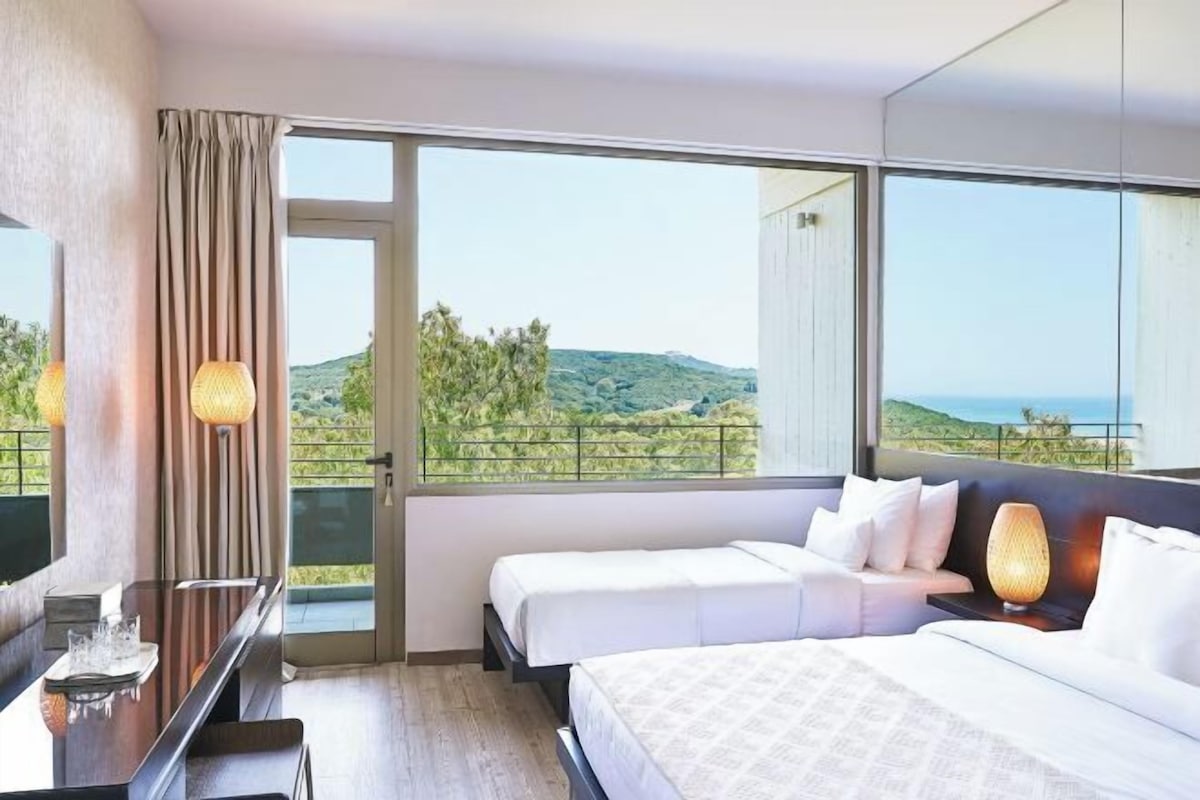 Une chambre d’hôtel équipée d’un lit, d’une table de chevet et d’une grande fenêtre donnant sur le paysage.