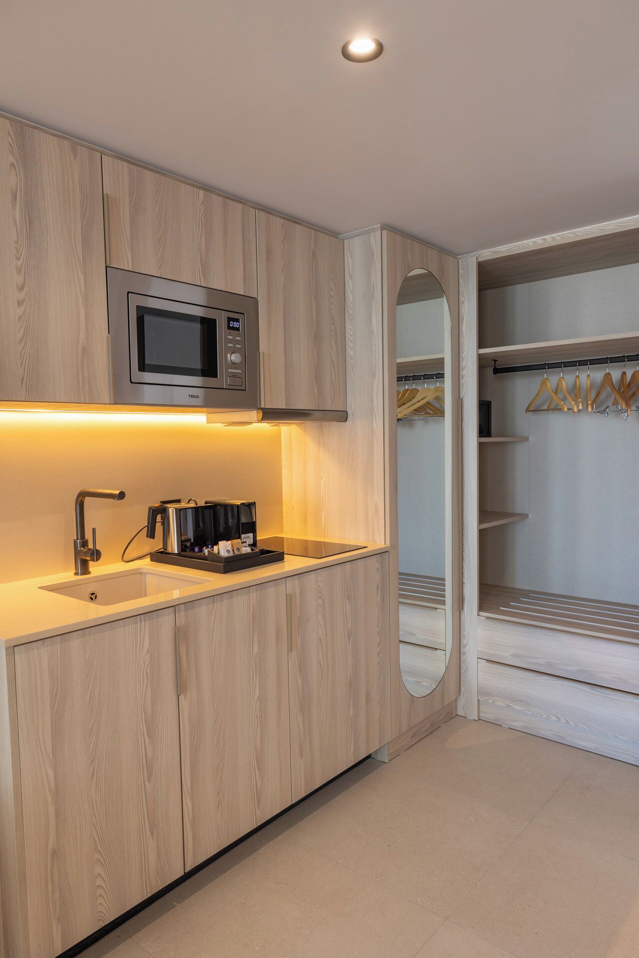 Una cocina moderna con armarios de madera, microondas integrado, cafetera y pileta.