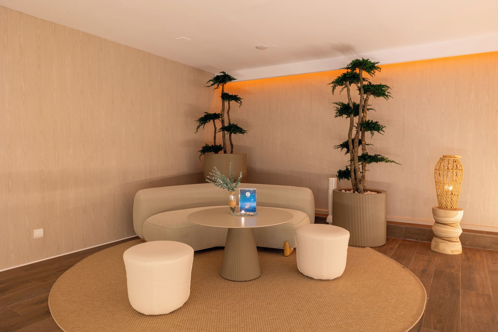 A modern room with a round table, two ottomans, and two tall potted plants.