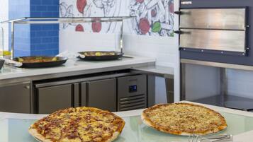 A kitchen with two pizzas on a glass counter, a pizza oven, and a wall with a fruit pattern.