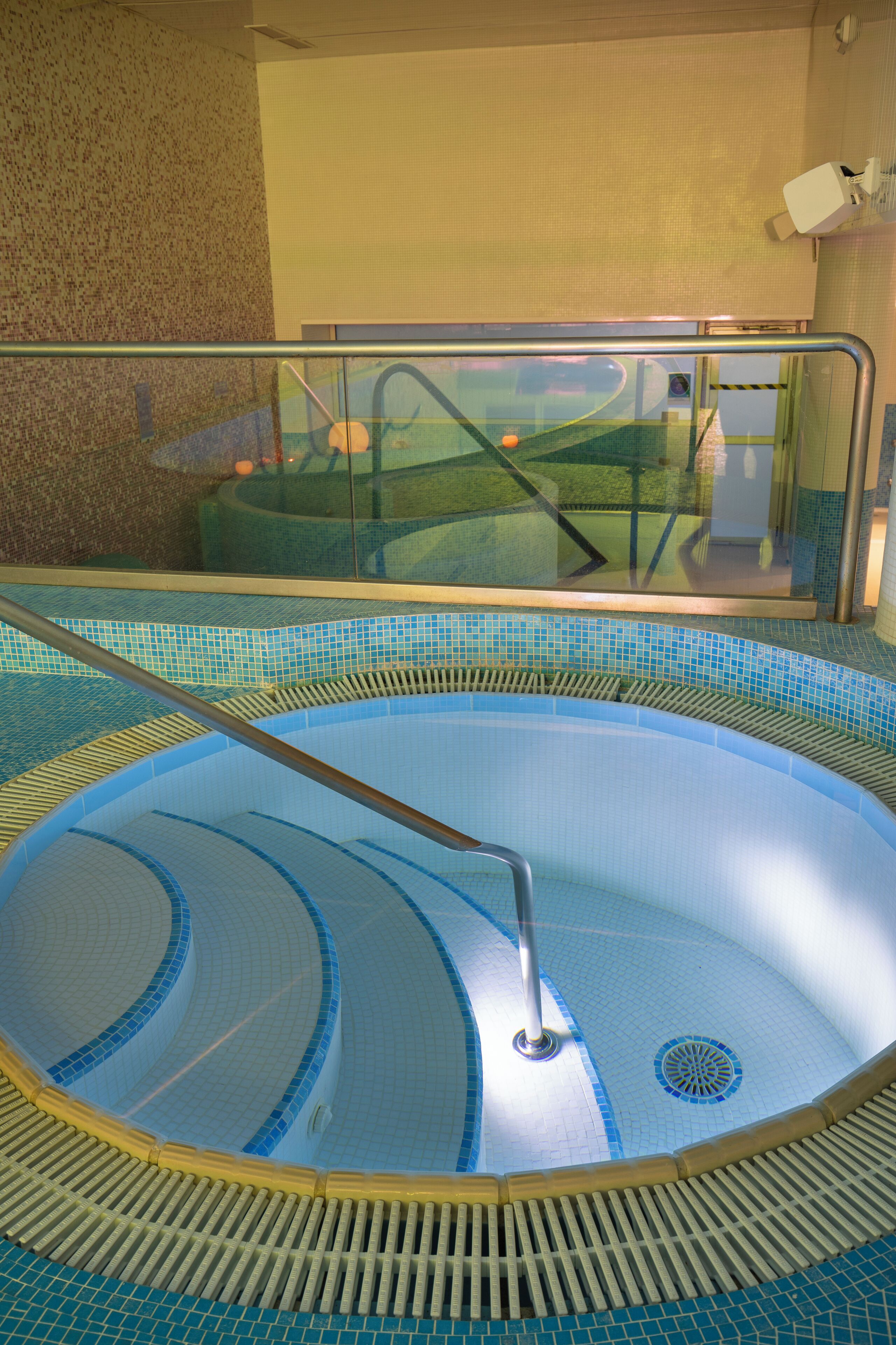 A circular indoor pool with a glass railing and a drain in the center.