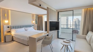 Une chambre d’hôtel moderne dotée d’un grand lit, d’une télévision, d’un canapé et d’un balcon offrant une vue sur la ville.