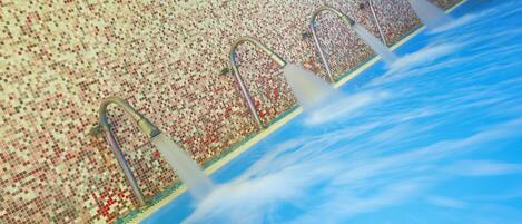 Ein Schwimmbecken mit drei Metallleitern und einer Wand aus Mosaikfliesen.