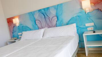 Habitación de hotel con una cama grande, ropa de cama blanca, una mesita de noche con lámpara y un cuadro abstracto azul en la pared.