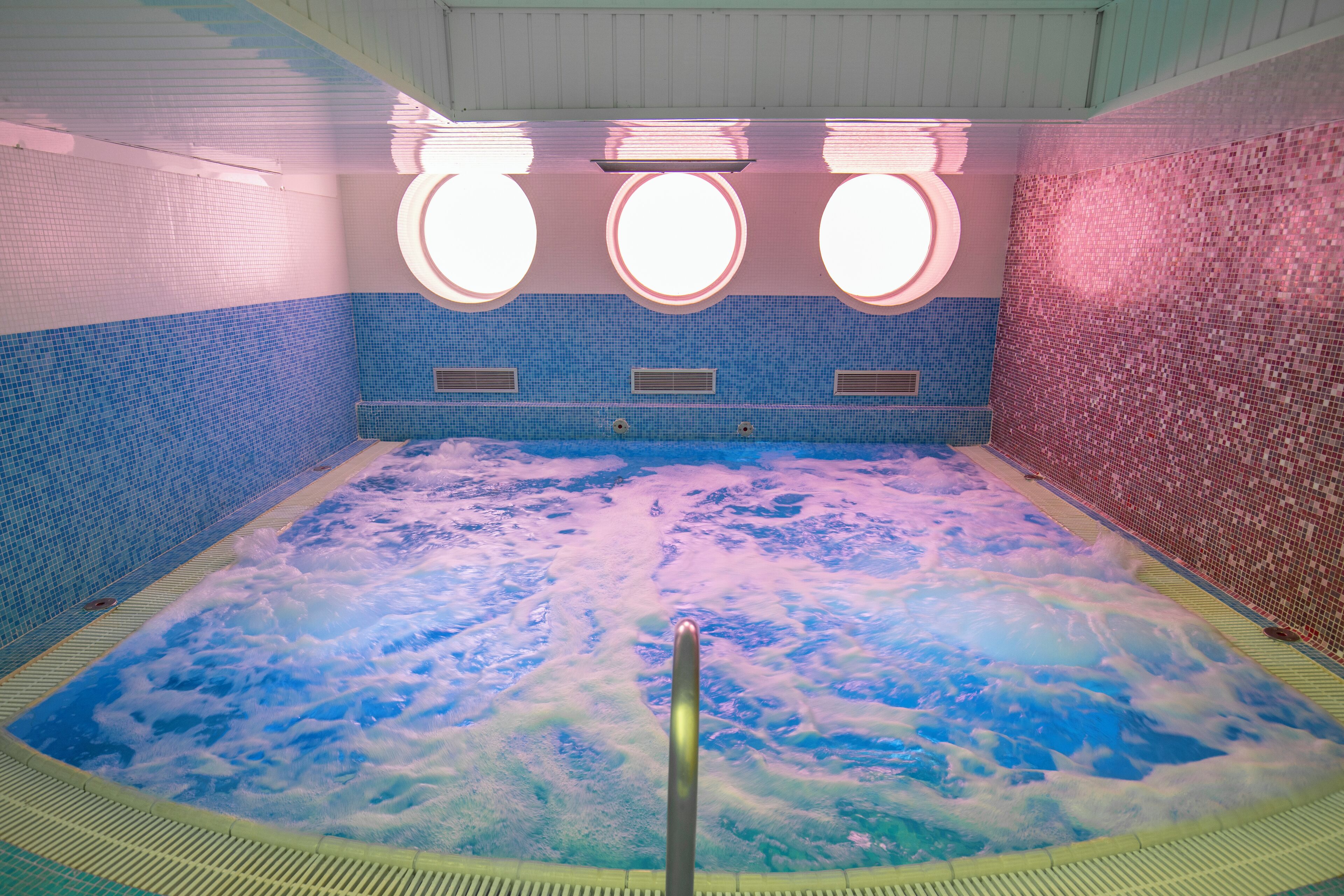 A hot tub with a view of the sky through the bubbles, surrounded by blue and pink mosaic tiles.