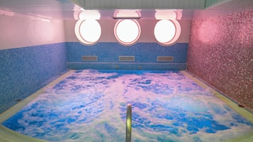 Ein Whirlpool mit Blick zum Himmel, durchzogen von Blasen, umgeben von blau-rosa Mosaikfliesen.