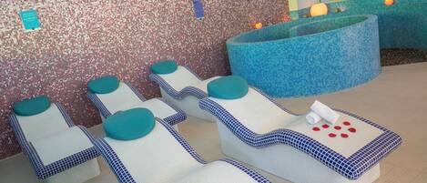 A spa area with multiple massage chairs, a large blue bathtub, and a mosaic wall.