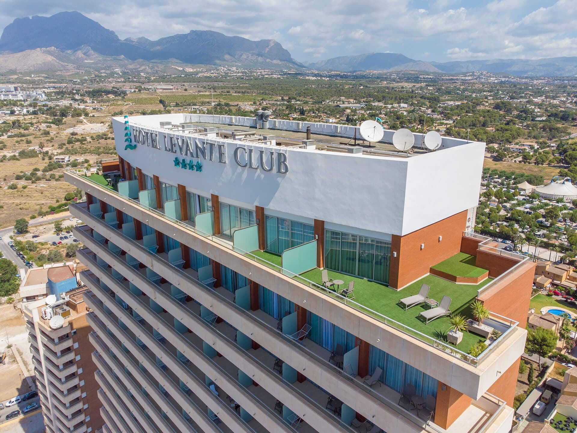 A high-rise hotel with multiple balconies, a rooftop terrace, and a view of the surrounding landscape.