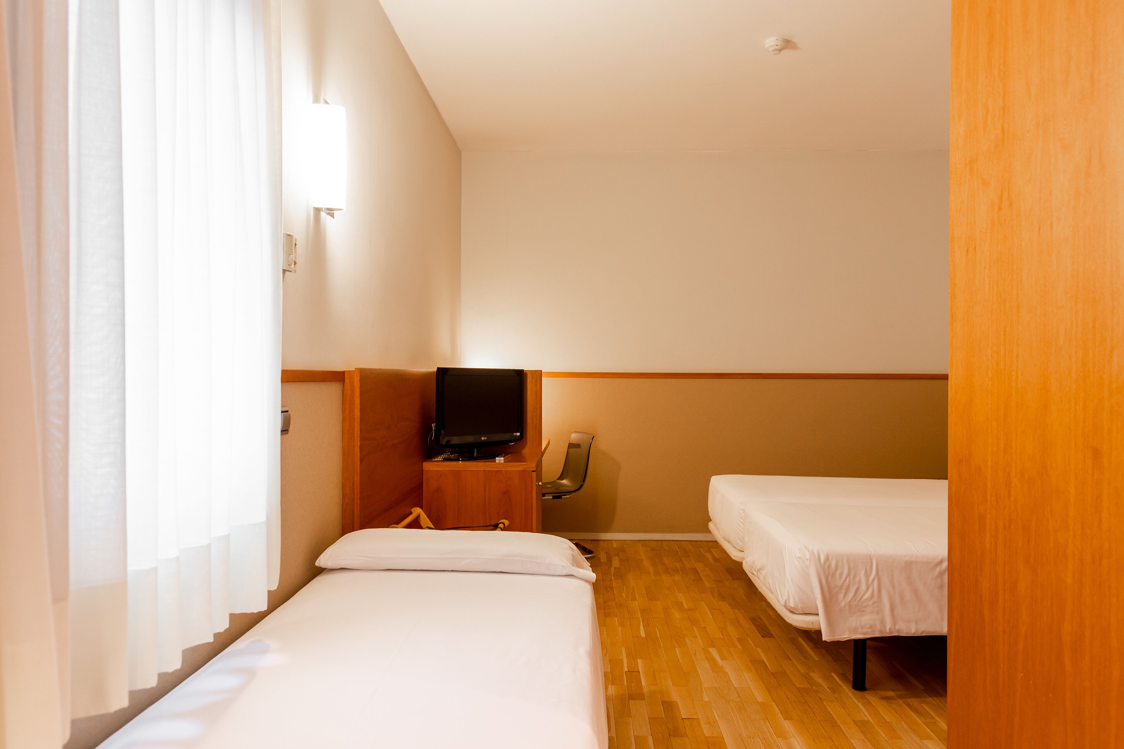Una habitación de hotel con dos camas, televisión y suelo de madera.