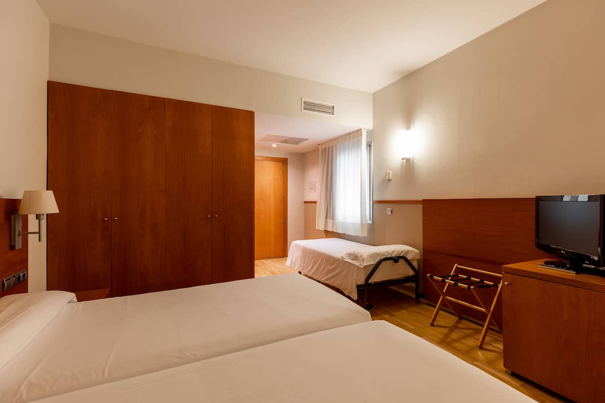 Habitación de hotel con dos camas, un armario de madera, un televisor y un escritorio pequeño.