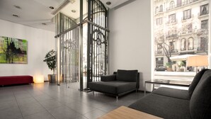 Een moderne lobby met een rode bank, grijze banken, een houten tafel en een groot raam met uitzicht op gebouwen.