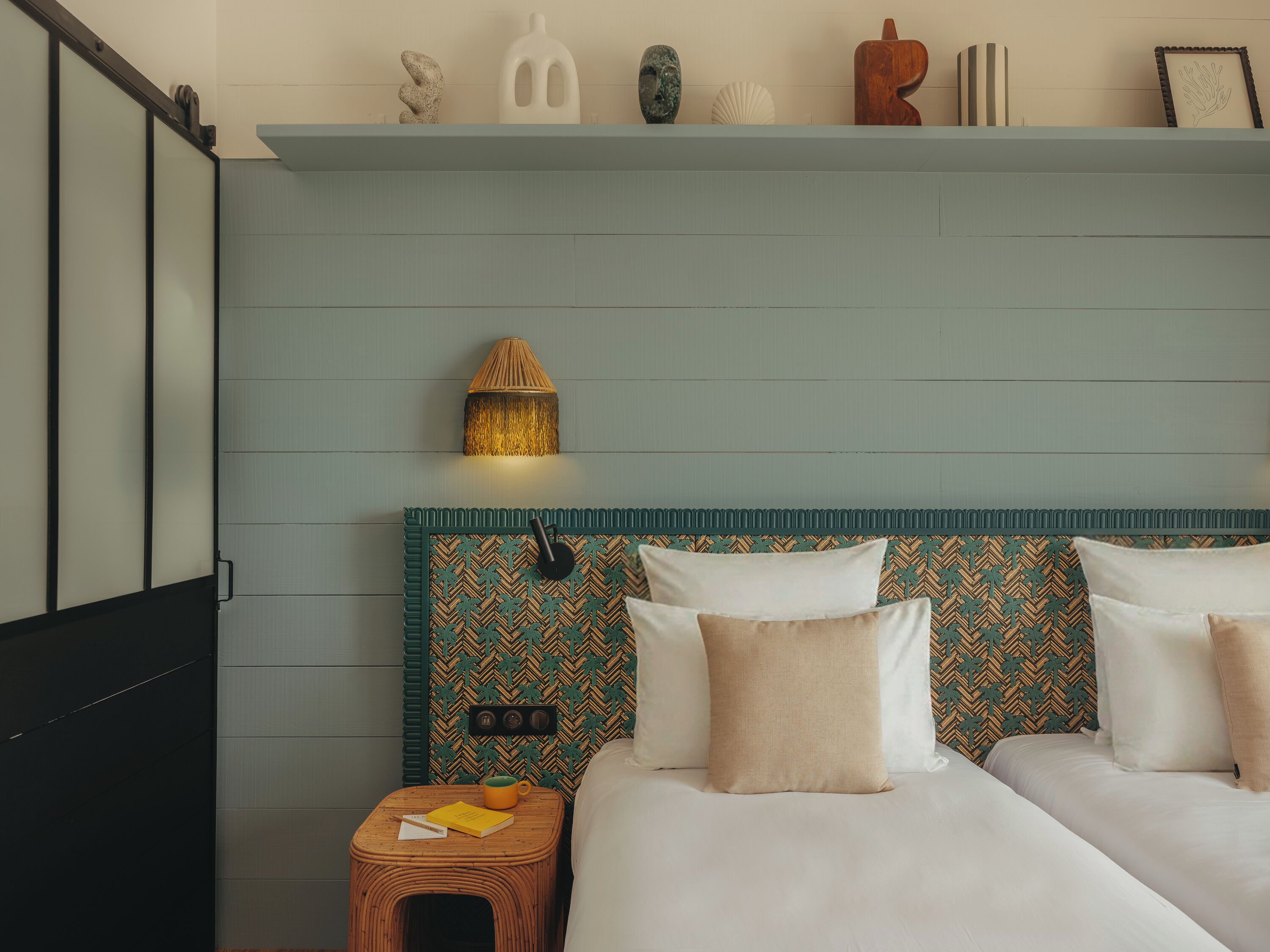 Quarto com cama, mesa de cabeceira, abajur e objetos decorativos em uma estante.