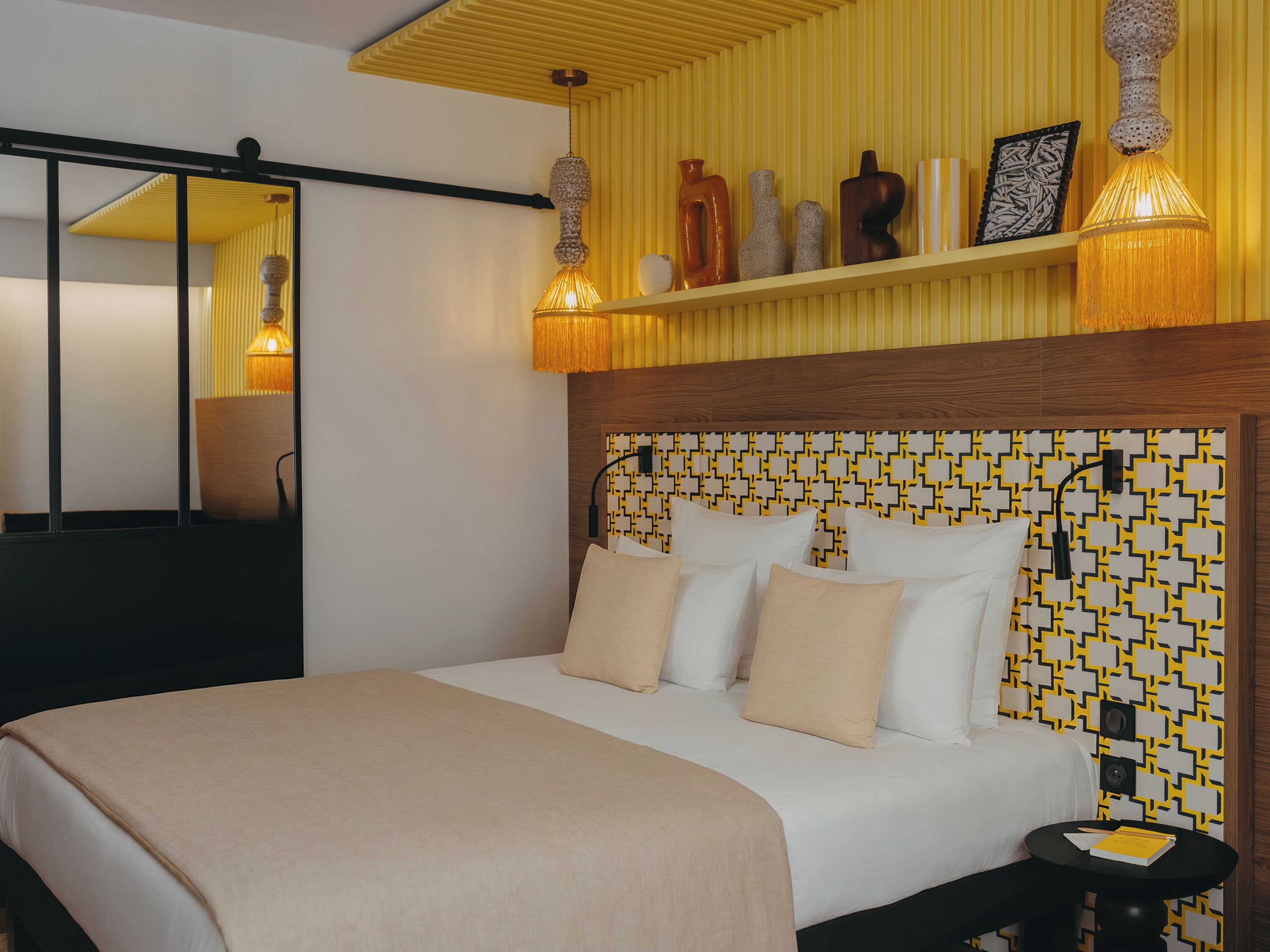 Une chambre d’hôtel avec un lit, une table de chevet et une étagère ornée d’objets décoratifs.