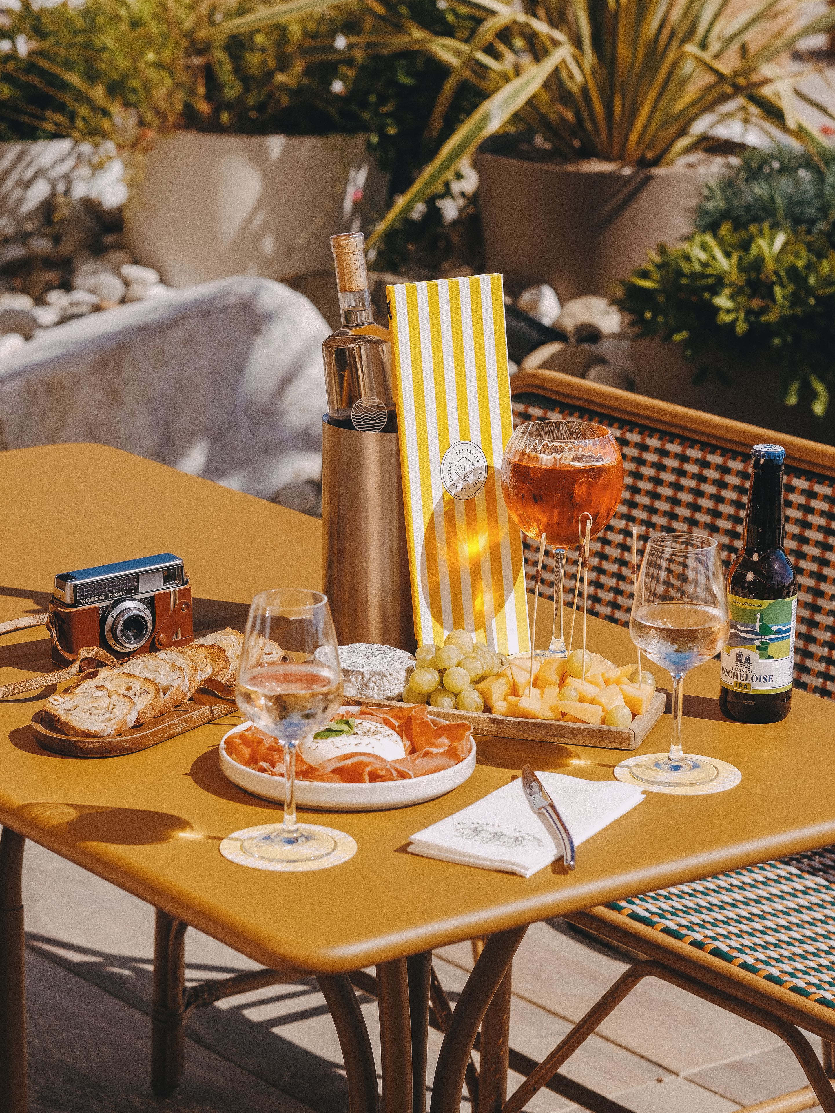 A table set with food and drinks, a camera, and a bottle of wine.
