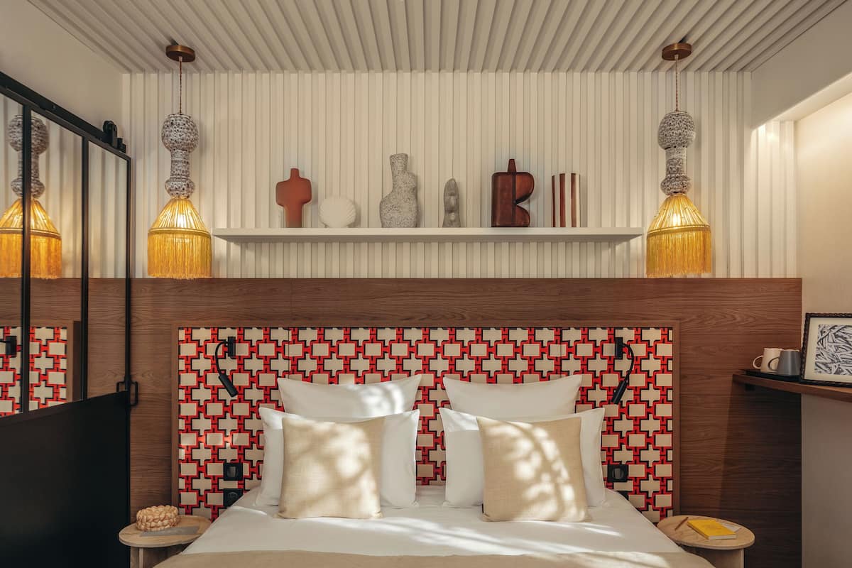 A modern bedroom with a patterned headboard, bedside tables with lamps, and a large mirror.