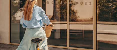 A person on a bicycle in front of a building with a sign reading 'LES BRISES HOTEL SUR L'OCEAN.'
