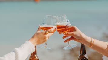 Deux personnes trinquent avec des verres à la main, une bouteille de Rochelais IPA et une bouteille de Cheloise sont posées sur une table blanche, près de la mer.