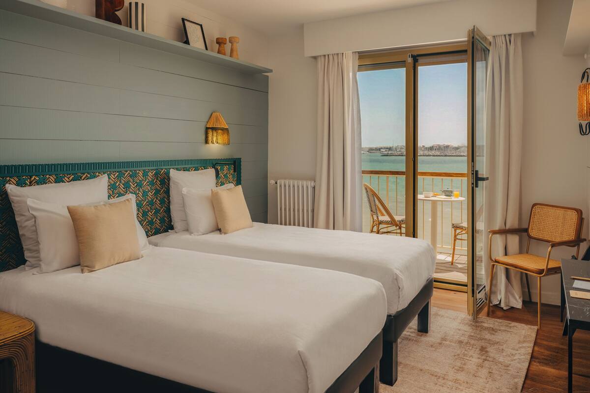 A hotel room with two beds, a balcony with a view, a small table, and a chair.