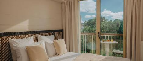 A hotel room with a large bed, a balcony with a table and chairs, and a view of trees.