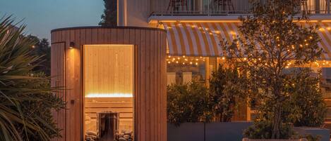 Un edificio moderno con fachada de madera, un balcón con sillas y una guirnalda de luces.