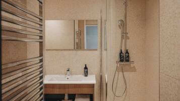 Un baño con ducha envuelta en vidrio, un lavamanos con espejo y un mueble de tocador de madera con toallas.