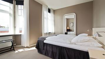 Une chambre à coucher avec un lit, une table de chevet, une lampe, un miroir et une fenêtre avec des rideaux.