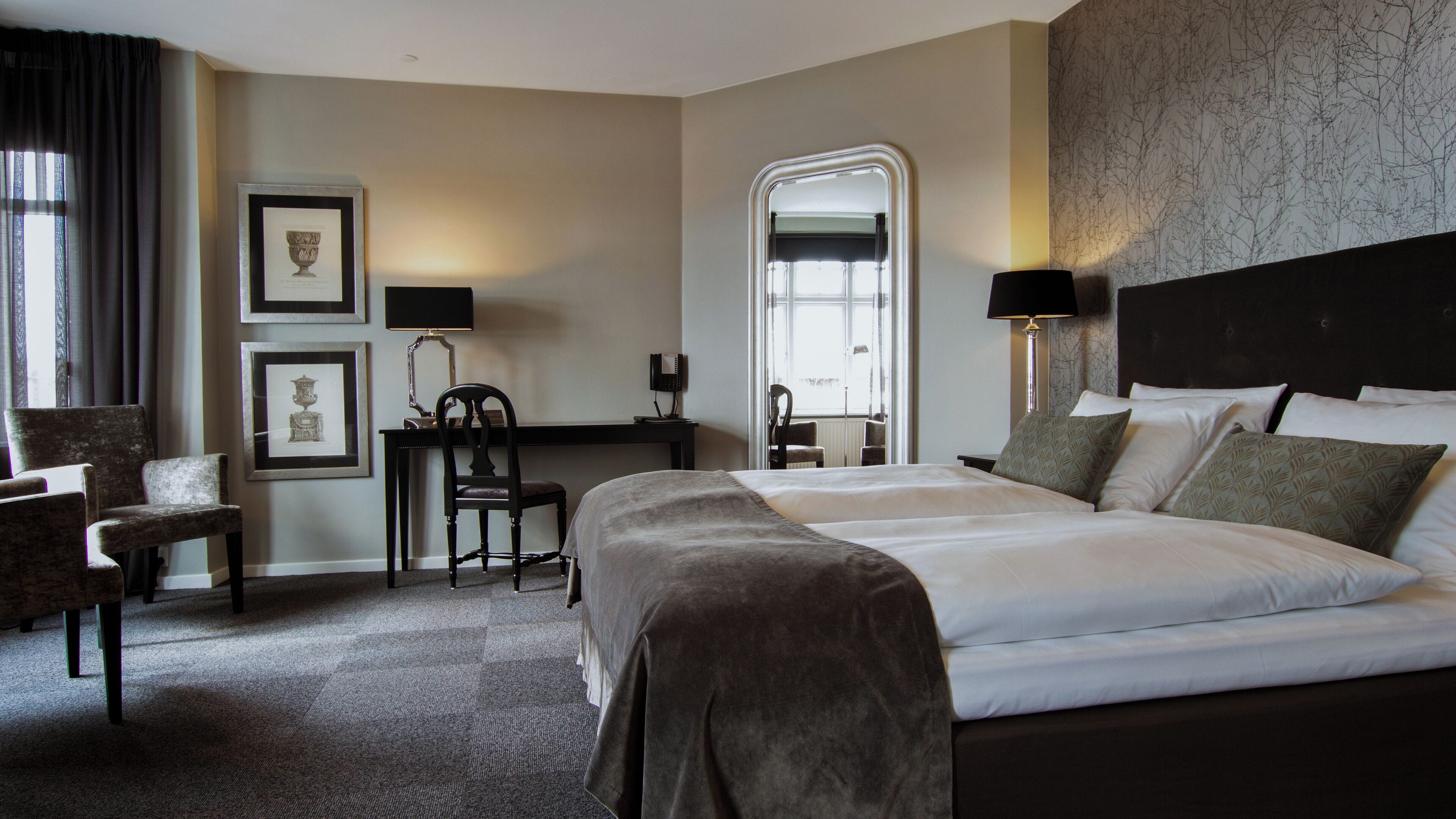 A hotel room with a large bed, a desk with a chair, a computer, and framed pictures on the wall.