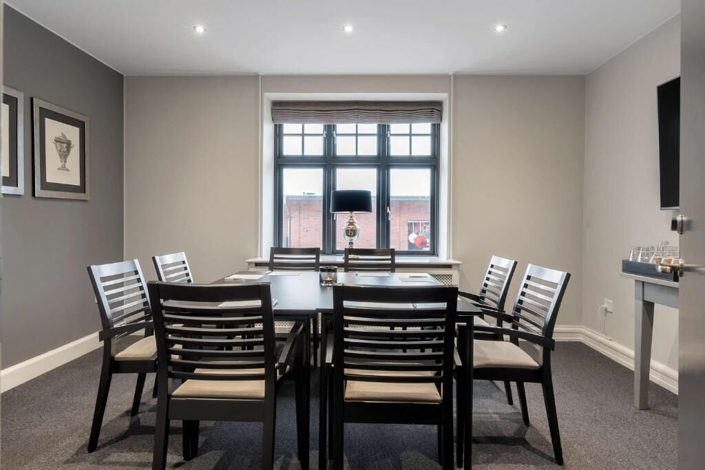 A dining area with a table and chairs, a window with blinds, and framed pictures on the wall.