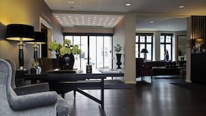 Un moderno hall de hotel con un piano, zona de estar y amplios ventanales.
