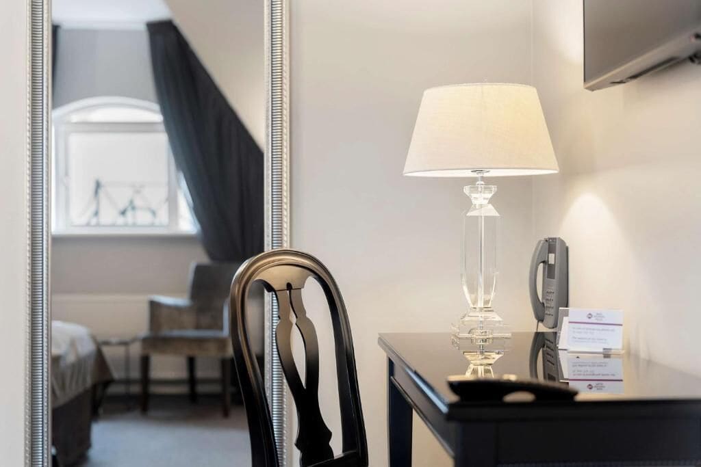 Habitación de hotel con una cama, una silla, un escritorio con lámpara, teléfono y televisor montado en la pared.