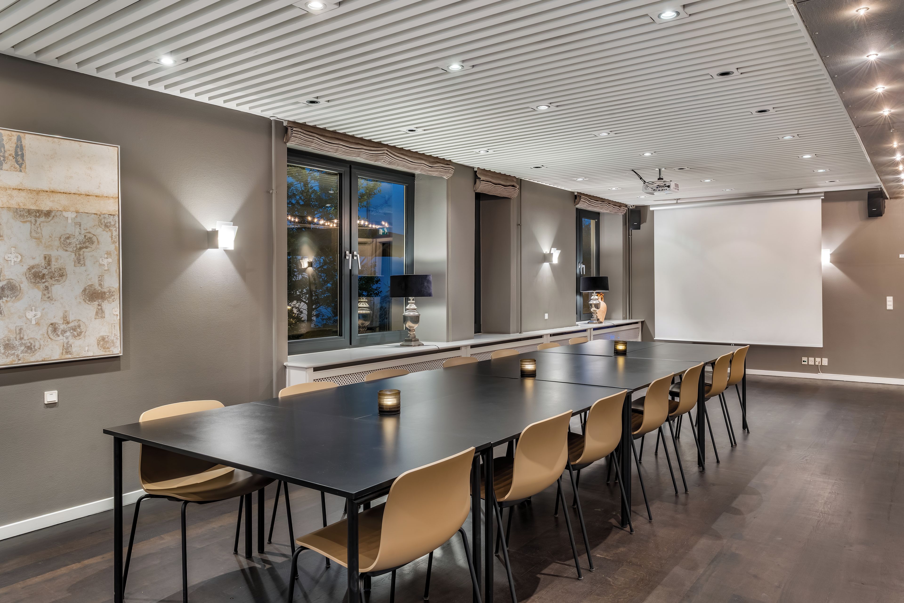 A conference room with a long table, chairs, a projector screen, and a large window with curtains.