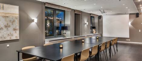 A conference room with a long table, chairs, a projector screen, and a large window with curtains.