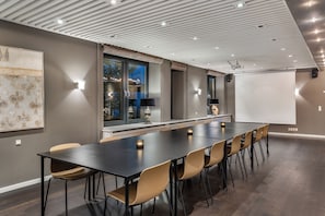 Un salón de conferencias con una larga mesa, sillas, una pantalla de proyector y un amplio ventanal con cortinas.