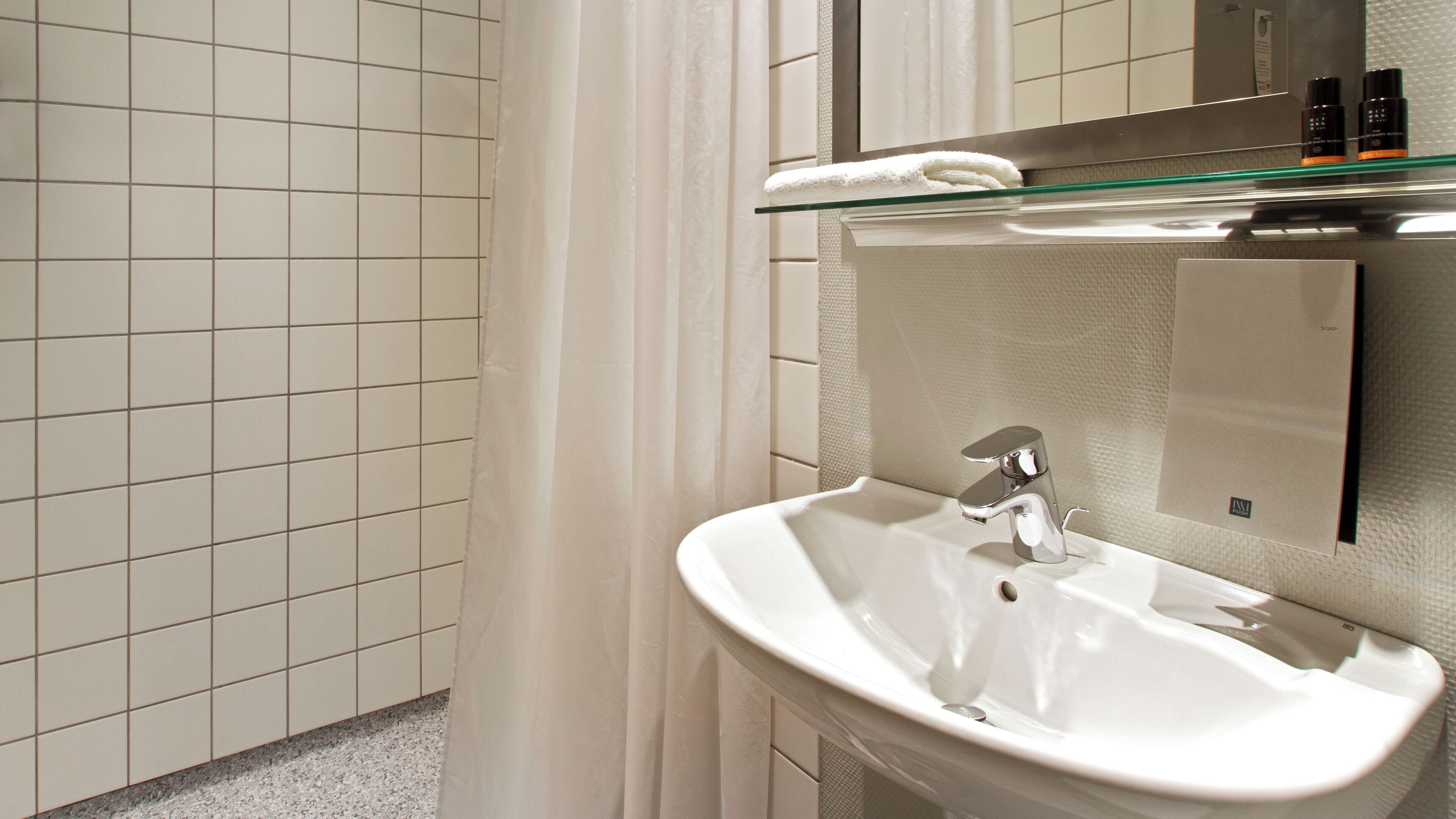 A bathroom with a white sink, a glass shelf with toiletries, and a mirror.