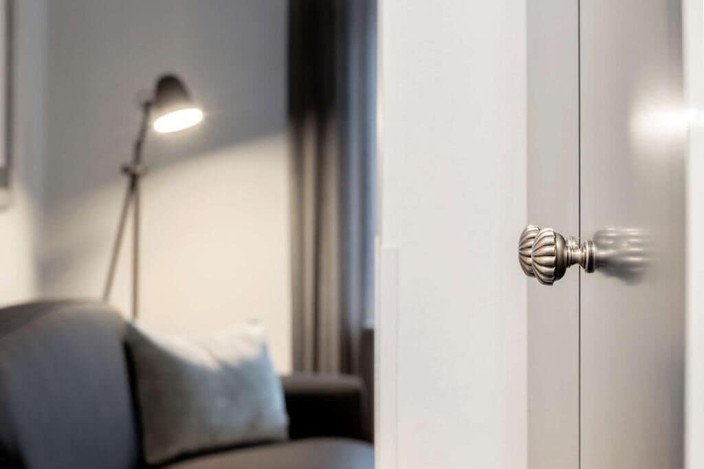 Una puerta con un picaporte metálico y una lámpara moderna al fondo.