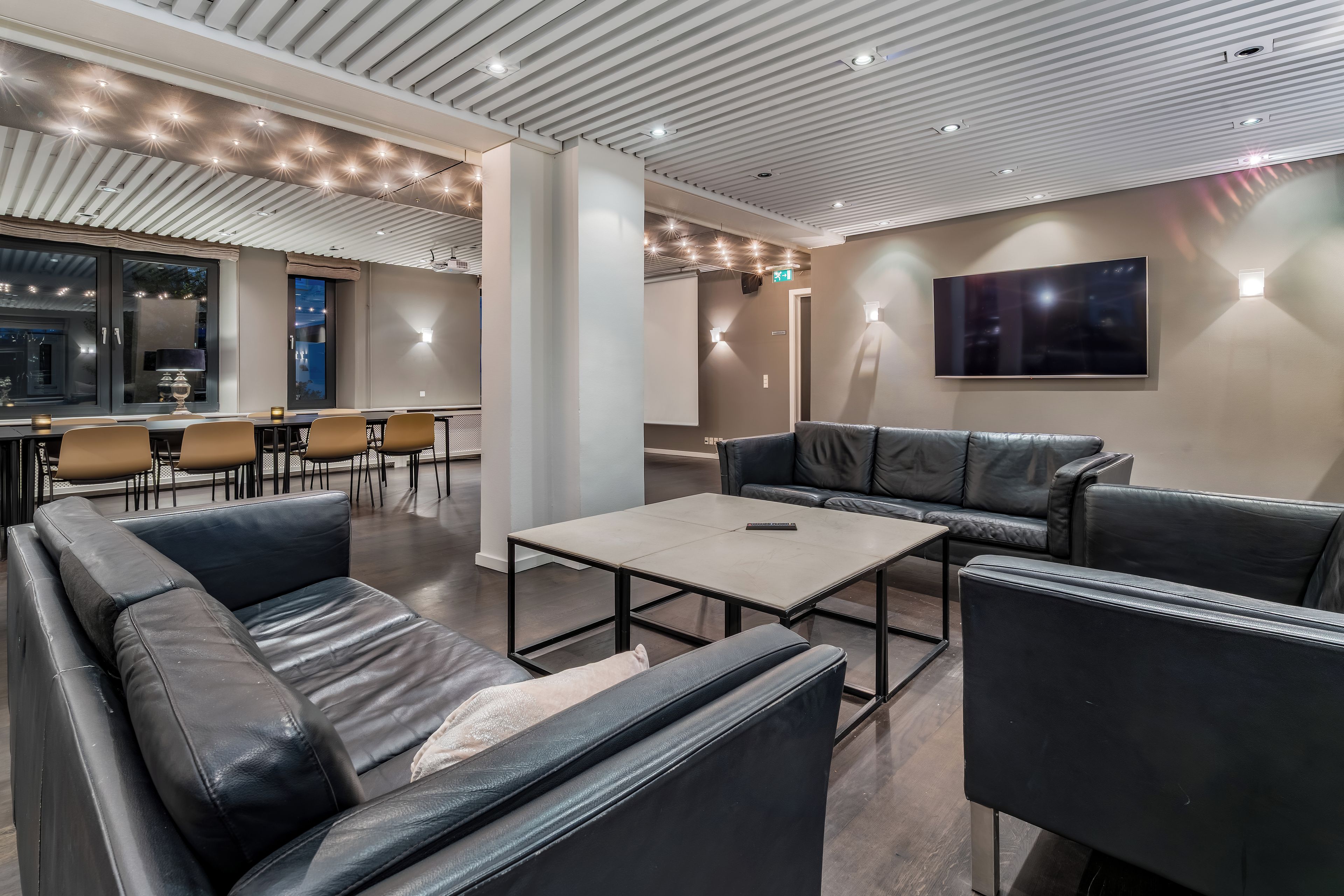 A modern lounge area with leather sofas, a coffee table, and a flat-screen TV mounted on the wall.